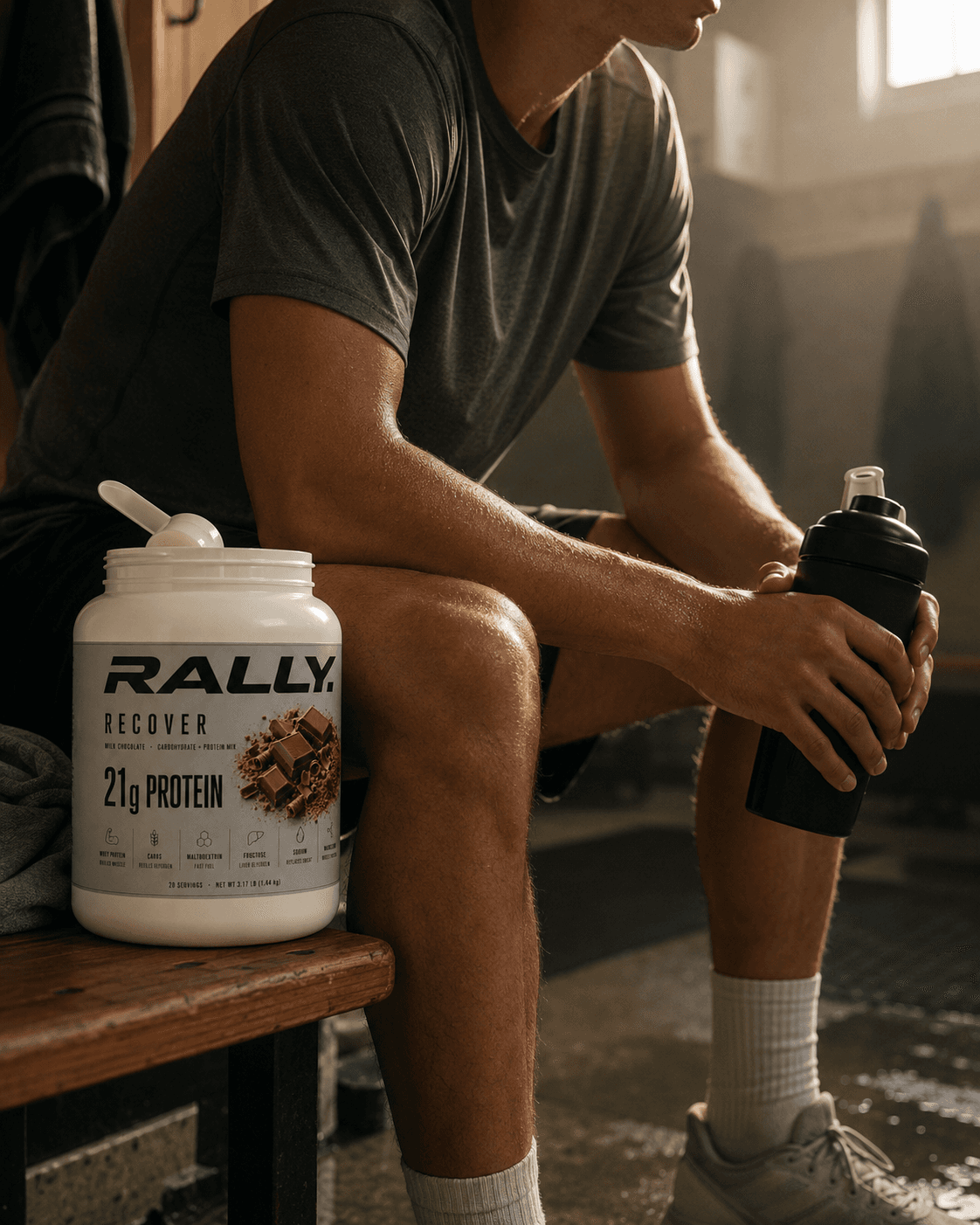 Athlete resting on a locker-room bench with a tub of RALLY RECOVER beside him